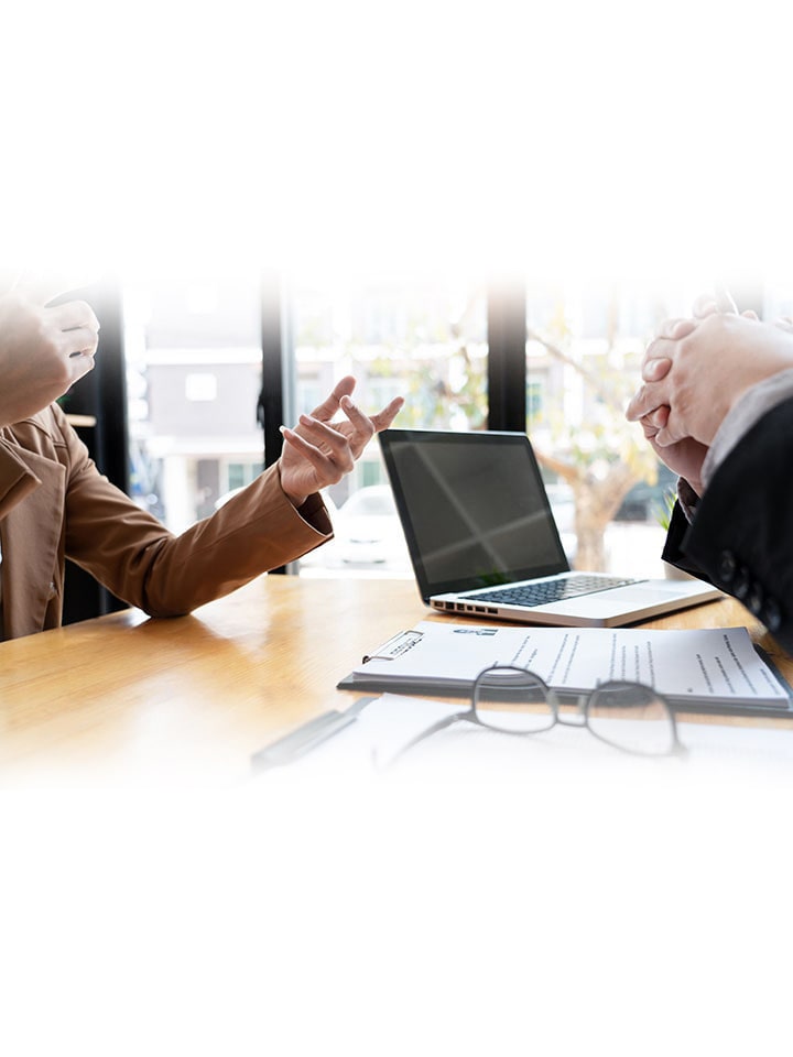 月刊 Routes の誌面イメージ写真（腕のみ見えているビジネスパーソンがパソコンと眼鏡、バインダー資料ののったデスクをはさんで会話しているシーンの切抜）